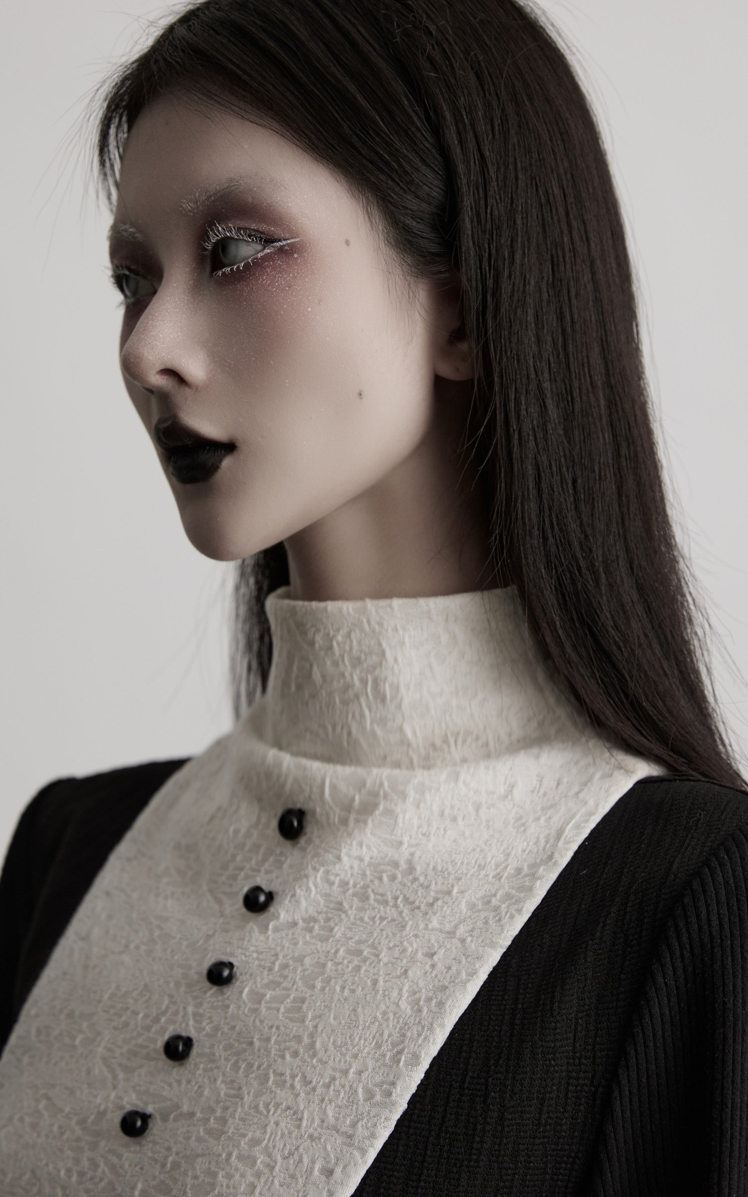 close-up of black high neck dress with textured contrast panel and buttons