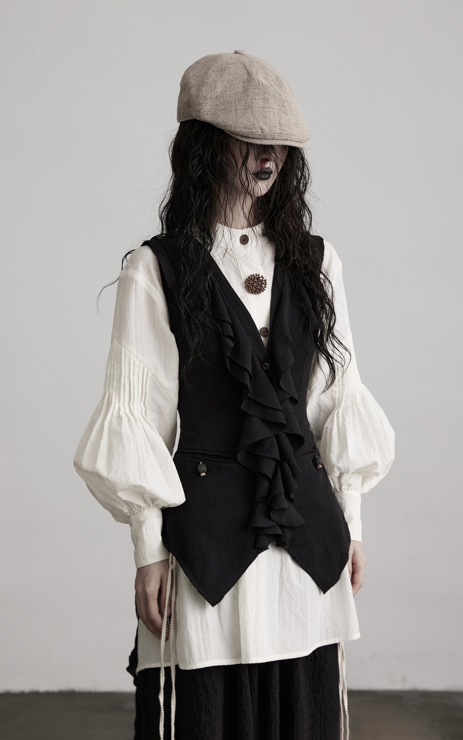 angled side view of black ruffled tie vest with layered front drape