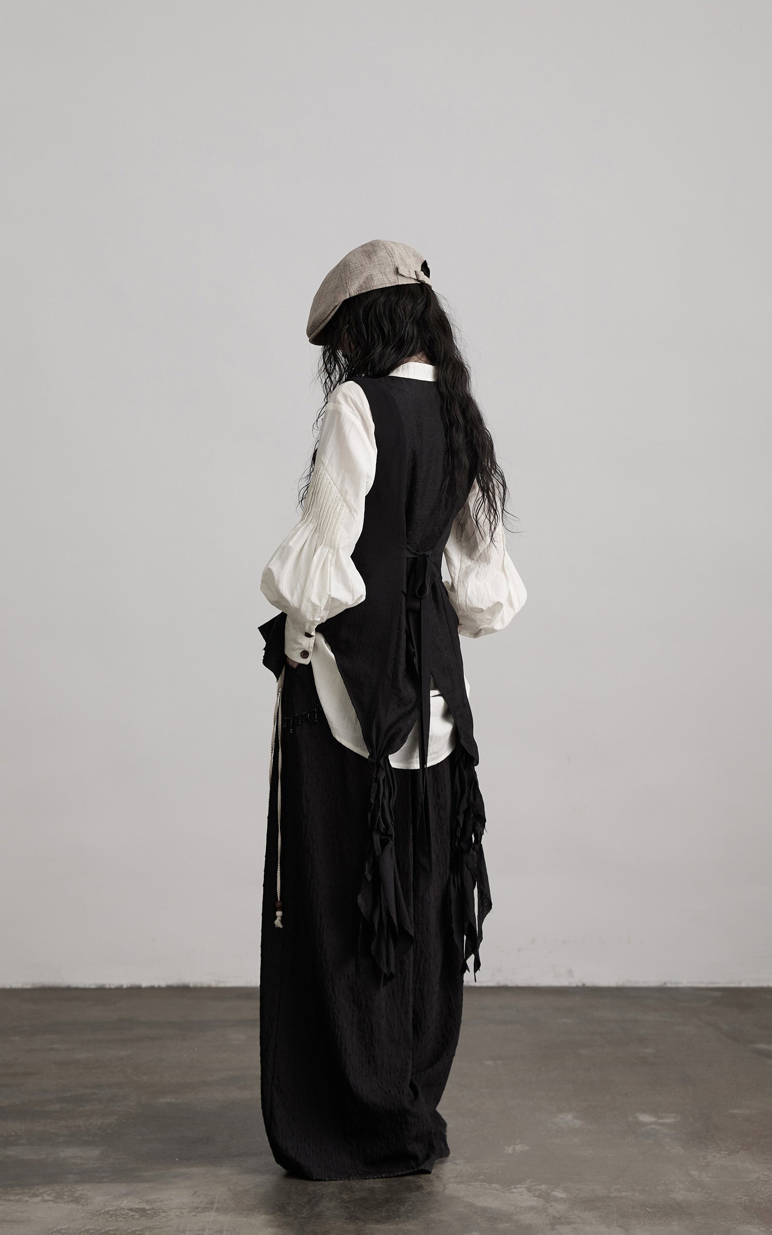 back view of black ruffled tie vest with draped tie details